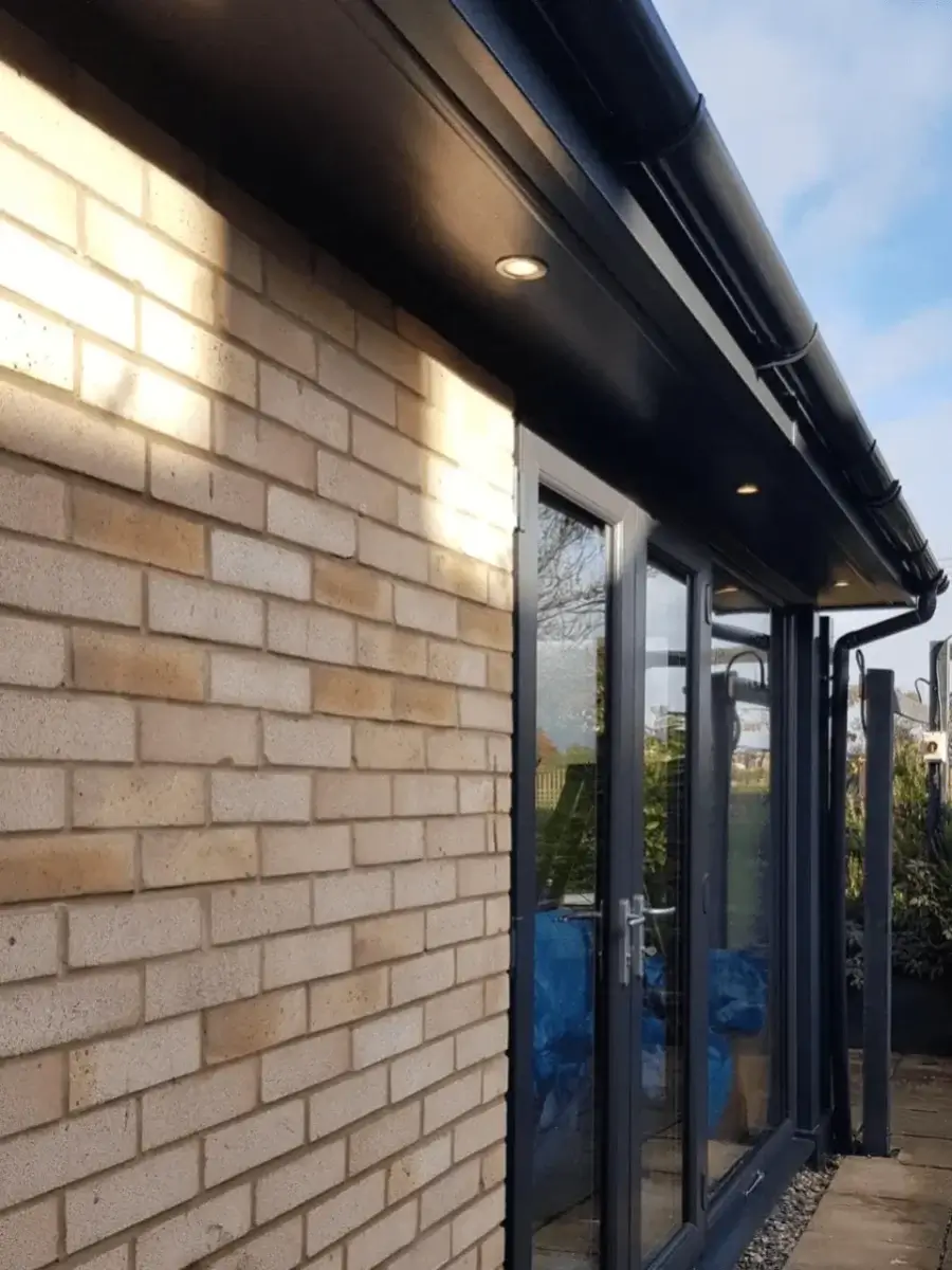 Close-up of a modern black uPVC ogee profile guttering and downpipe system installed on a light brick home by Norfolk Exterior Solutions